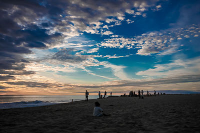 People on beach against sky during sunset