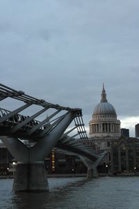 Millennium bridge over thames river by st paul cathedral against sky