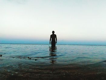 Silhouette man standing in sea against clear sky