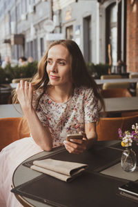 Young woman using phone while sitting on table