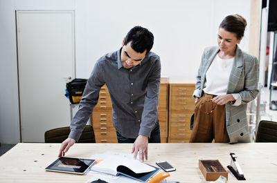 Businessman reading file and showing digital tablet to coworker at table in meeting