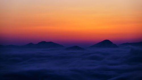 Scenic view of silhouette mountains against orange sky