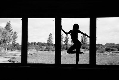 Silhouette woman standing by window against sky