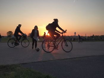 People riding bicycles with woman against clear sky during sunset