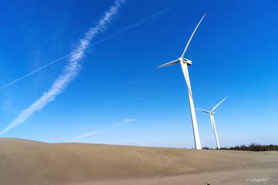 Low angle view of wind turbines on landscape against blue sky
