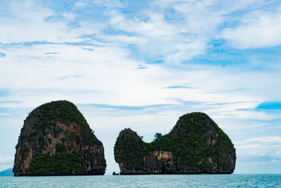 Scenic view of rock island in calm sea against cloudy sky