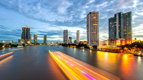 Light trails on city by buildings against sky