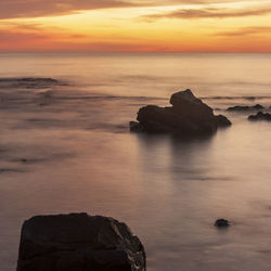 Rock formation on sea against sky during sunset