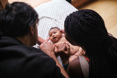 High angle caring african american mom changing diapers on infant lying on blanket with hispanic dad