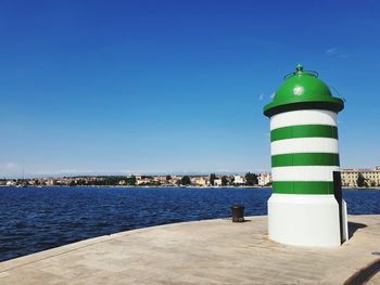 Lighthouse by sea against buildings in city