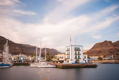 Sailboats moored in harbor by buildings against sky