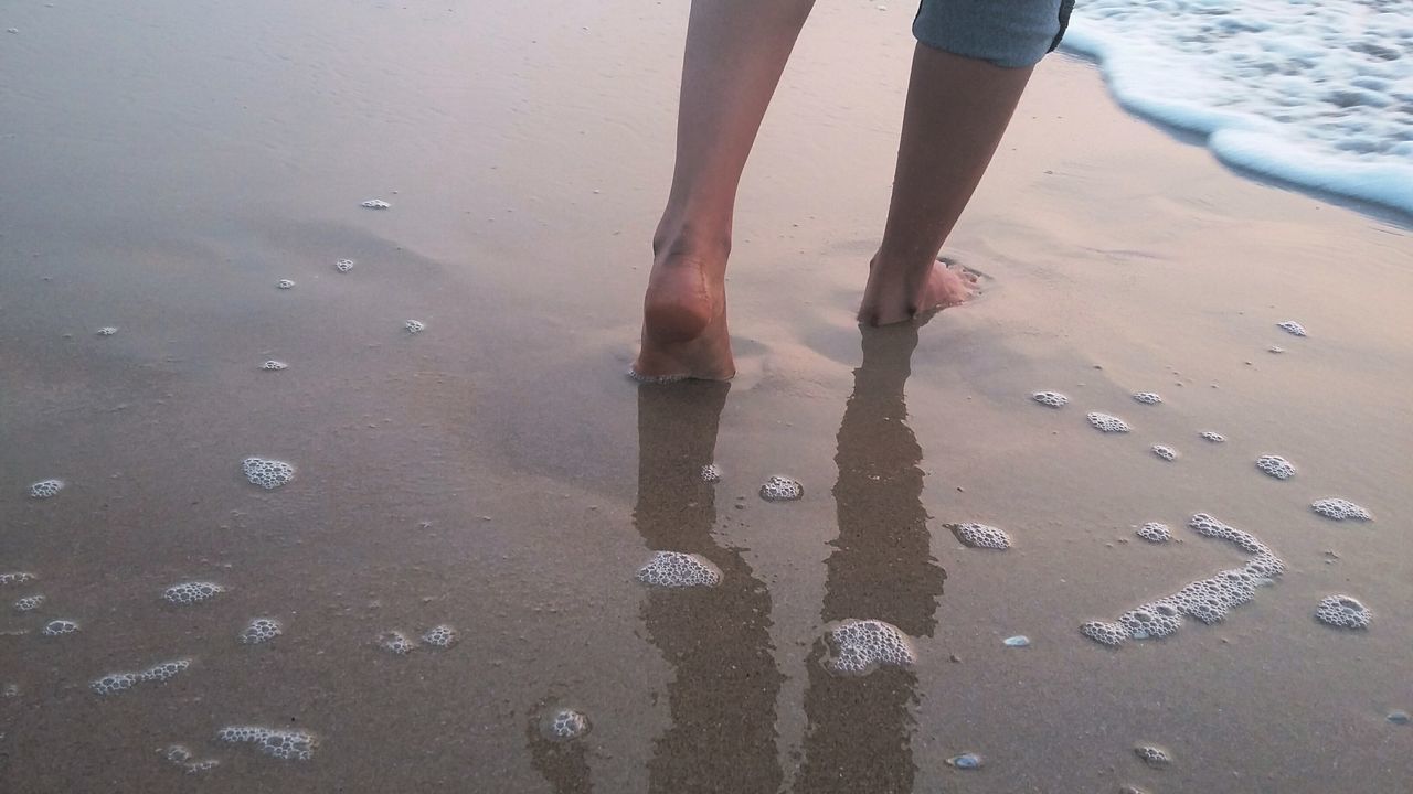 LOW SECTION OF MAN STANDING ON WET SHORE