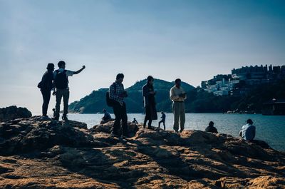 People standing on rock by sea against sky