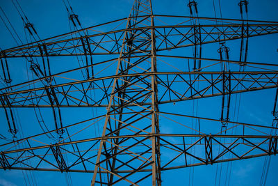 Low angle view of electricity pylon against blue sky