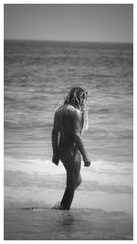 Naked man with long hair standing in sea