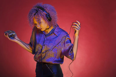 Woman with curly hair listening music against red background