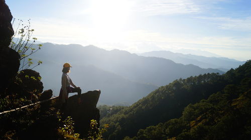 Man sitting on mountain against sky