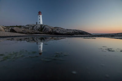 Lighthouse on beach by sea against clear sky