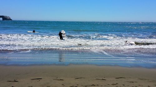 People on surfing in sea against clear sky