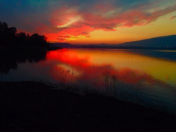Scenic view of lake against dramatic sky during sunset