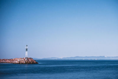 Lighthouse by sea against clear sky