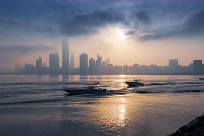 Sea by modern buildings against sky during sunset