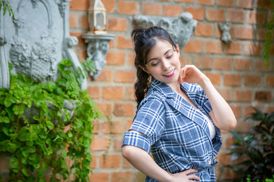 Smiling young woman standing against brick wall