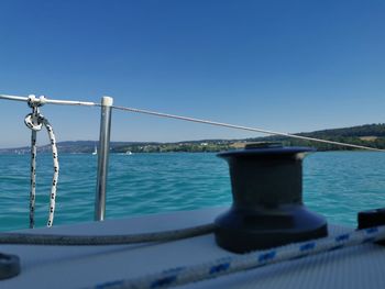 Railing by sea against clear blue sky