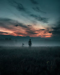 Silhouette man standing on field against sky during sunset