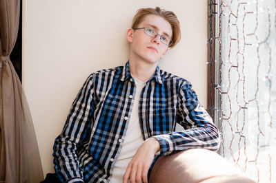 Portrait of young woman sitting against wall at home