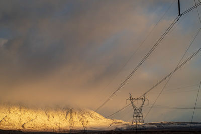 Low angle view of electricity pylon against sky during sunset