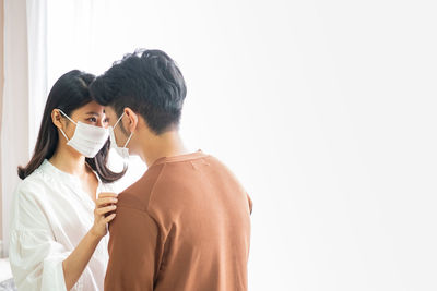 Young couple wearing mask kissing against white wall