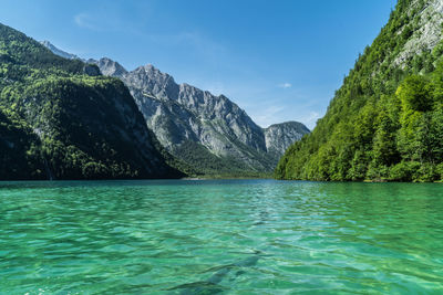 Scenic view of sea by mountains against blue sky