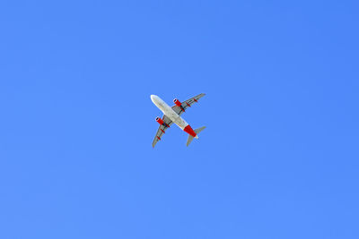 Low angle view of airplane flying against clear blue sky