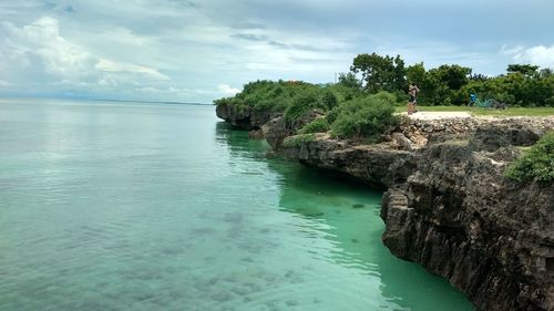 Scenic view of sea by cliff against cloudy sky