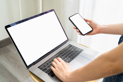 Midsection of man holding smart phone while using laptop