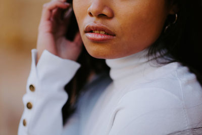 Cropped unrecognizable ethnic female in casual clothes standing in park while touching hair