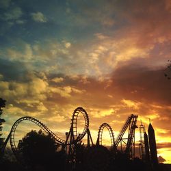 Silhouette rollercoaster against cloudy sky during sunset