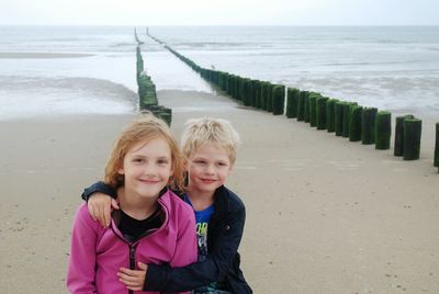 Portrait of smiling girl with brother sitting at beach