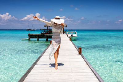 Woman wearing hat while standing on pier over sea against sky