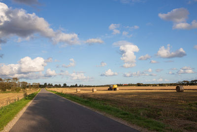 Empty road amidst agricultural field against sky