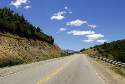 Empty road by trees against sky