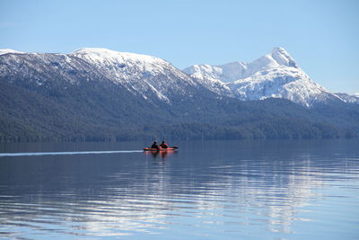 People kayaking on lake against mountains