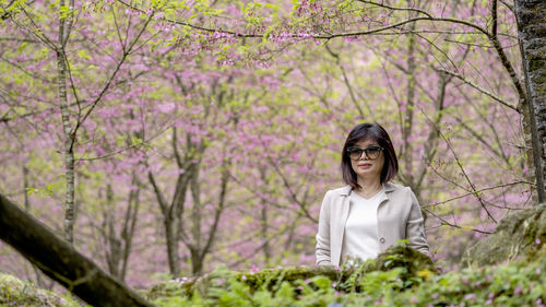 Portrait of young woman with pink flower against trees