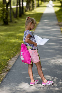 Side view of girl reading book while standing on walkway
