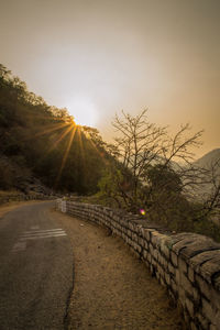 Road by trees against sky during sunset