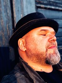 Close-up of man with eyes closed wearing hat against wall