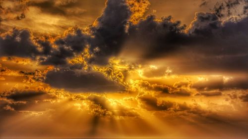 Low angle view of sunlight streaming through clouds during sunset