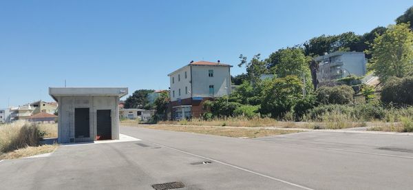 Road by buildings against clear blue sky