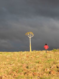 Woman walking on land against cloudy sky